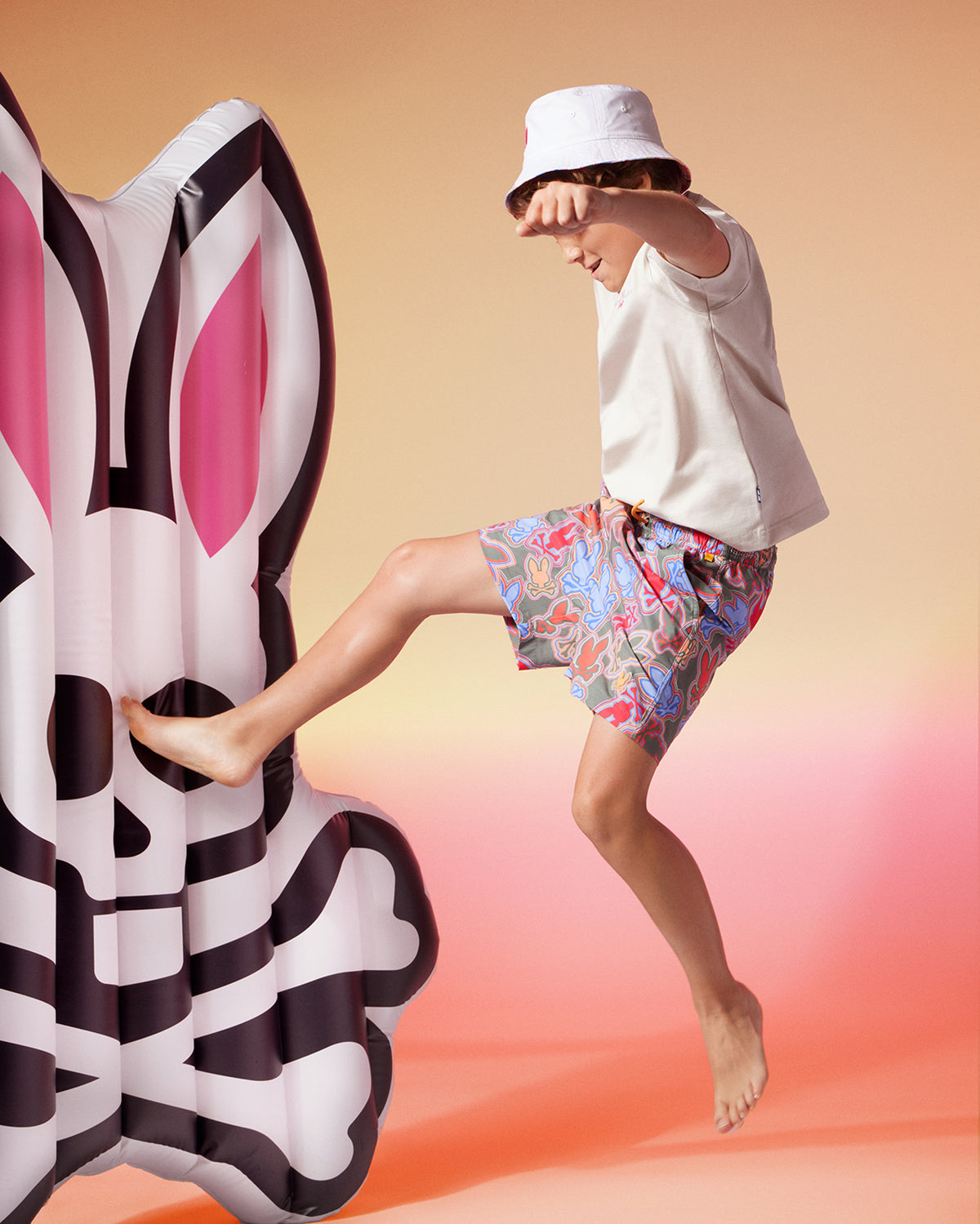 A child kicking a large Psycho Bunny pool floatie shaped like a POOL FLOATIE - B6A386B200, having fun at the resort vacation.