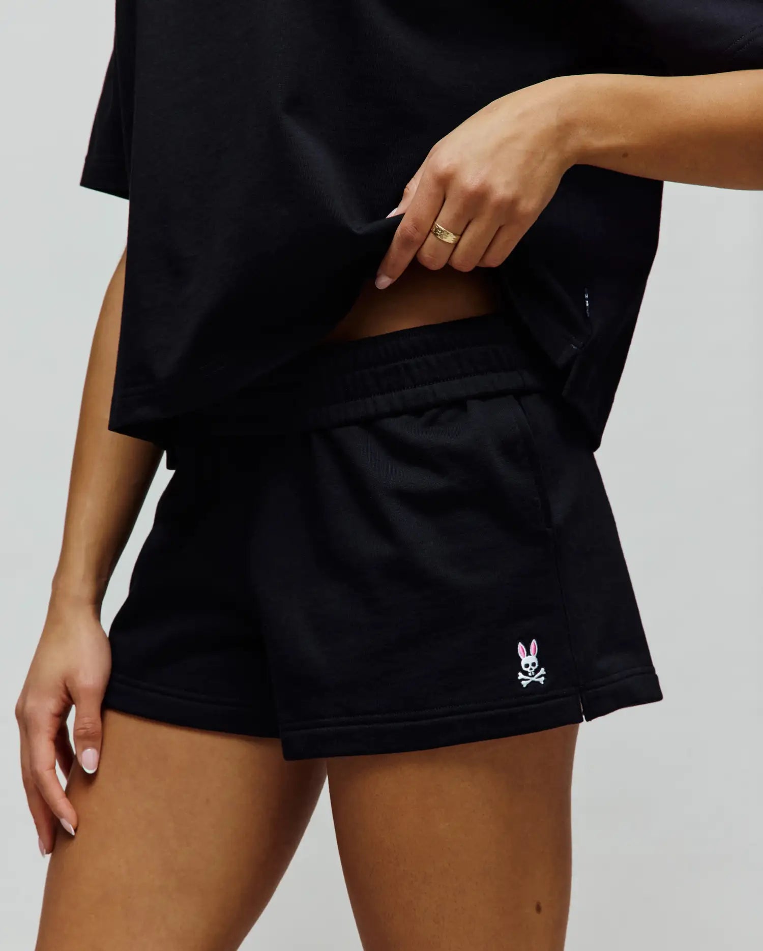 Womens Olivia Fleece Short, black relaxed-fit fleece shorts featuring an elastic waistband, side pockets, and a small embroidered white skull with pink bunny ears Psycho Bunny logo on the left hem.