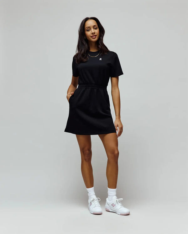 Womens Penelope Dress, black short sleeve crew neck with a relaxed fit, smooth jersey knit, drawstring waist, side pockets, and a small white embroidered Psycho Bunny skull logo on the left chest.