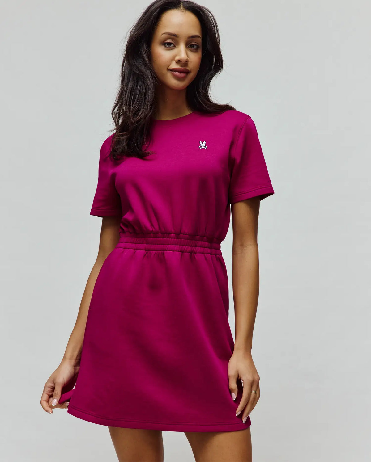Womens Penelope Dress in magenta, with a relaxed fit, short sleeves, crew neck, drawstring waist, and a small white embroidered Psycho Bunny skull logo on the left chest, made from soft jersey fabric.