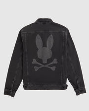 A black Psycho Bunny MENS PATHE DENIM JACKET - B6J741X1CO with a large, faded bunny graphic on the back depicting a bunny head above two crossed bones. The jacket features a button-up front, adjustable cuffs, and visible stitching accentuating the seams and edges. The background is plain white.