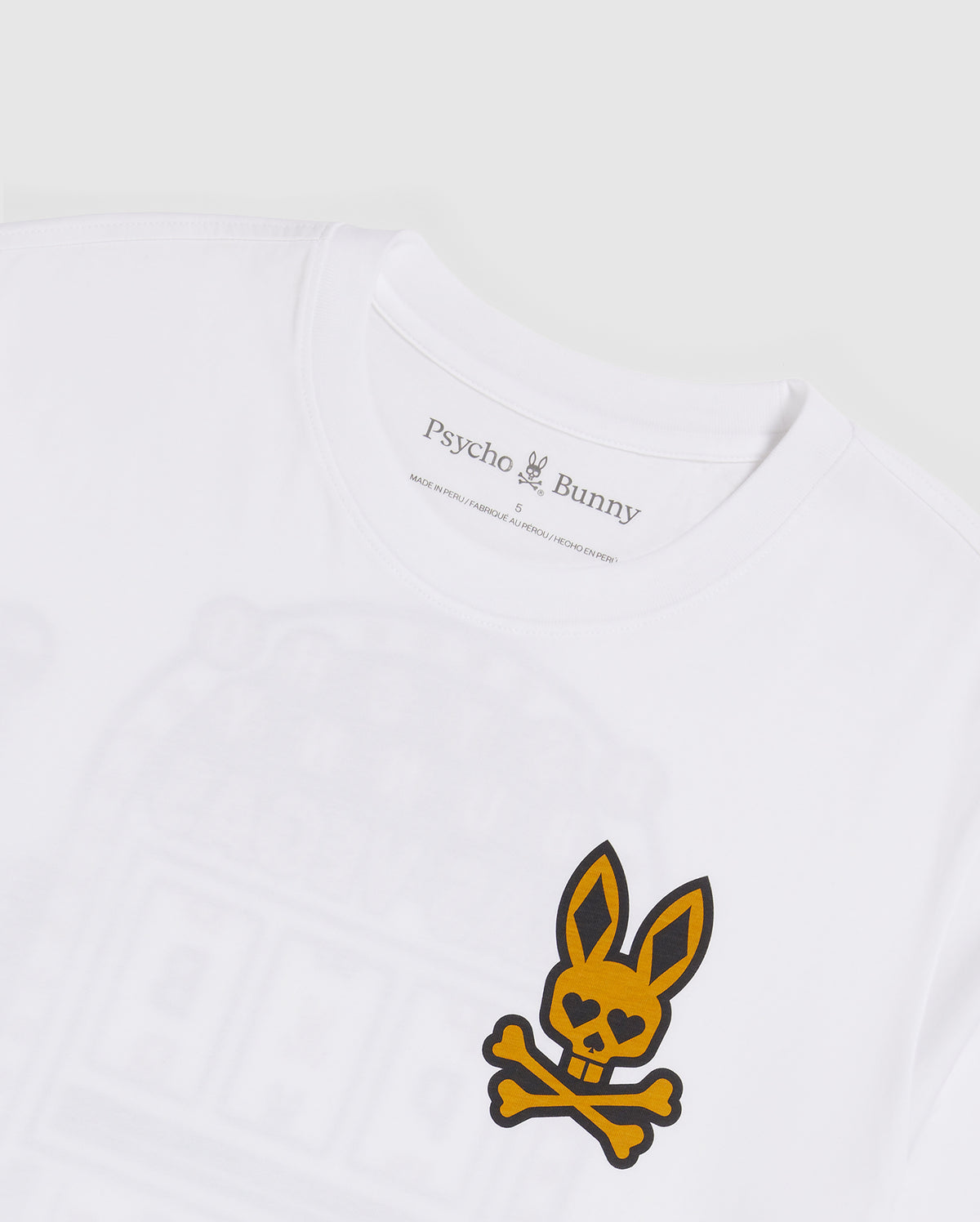 A close-up of a white Pima cotton jersey t-shirt with a yellow and black skull and crossbones logo featuring bunny ears on the chest. The inside label reads "Psycho Bunny" with a small printed bunny logo. The background is plain white. The product shown is the MENS VEGAS CITY TEE - B6U967X1PC by Psycho Bunny.